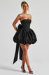 Woman wearing a black strapless dress with a ruffled skirt on a light gray background