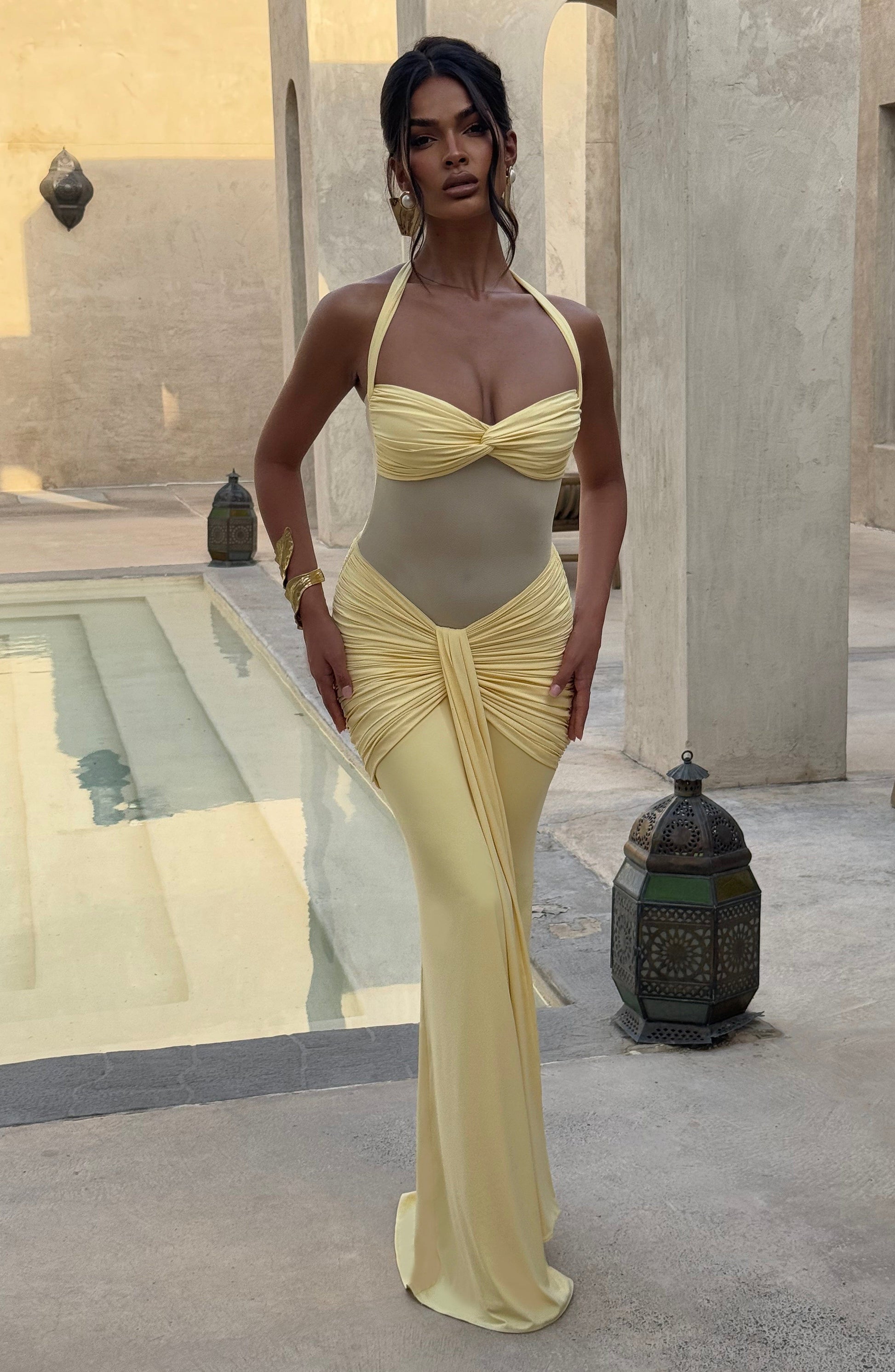 Woman in a yellow dress standing in an outdoor setting with architectural elements.