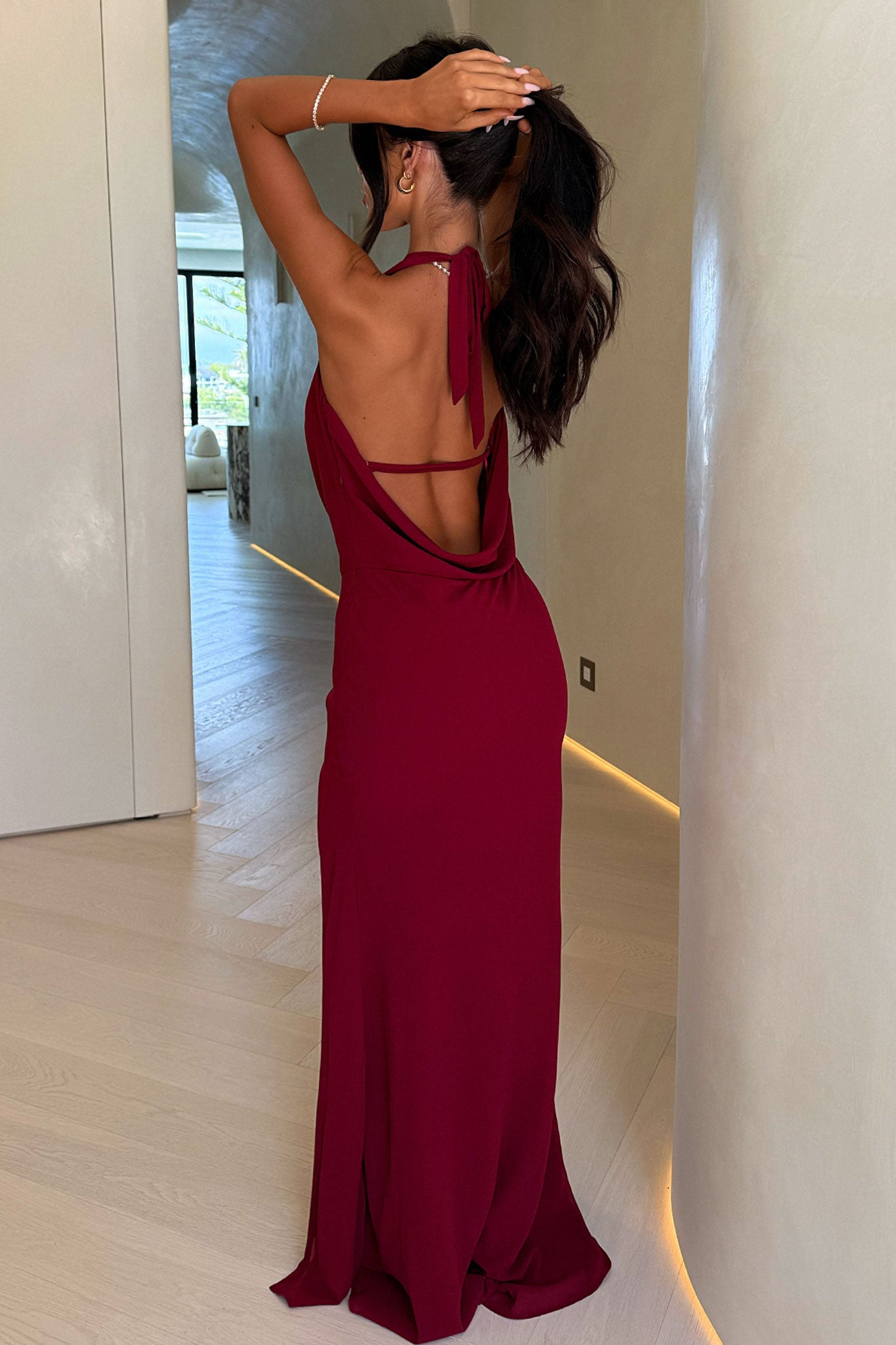 Woman in a burgundy evening gown standing in a modern interior setting.