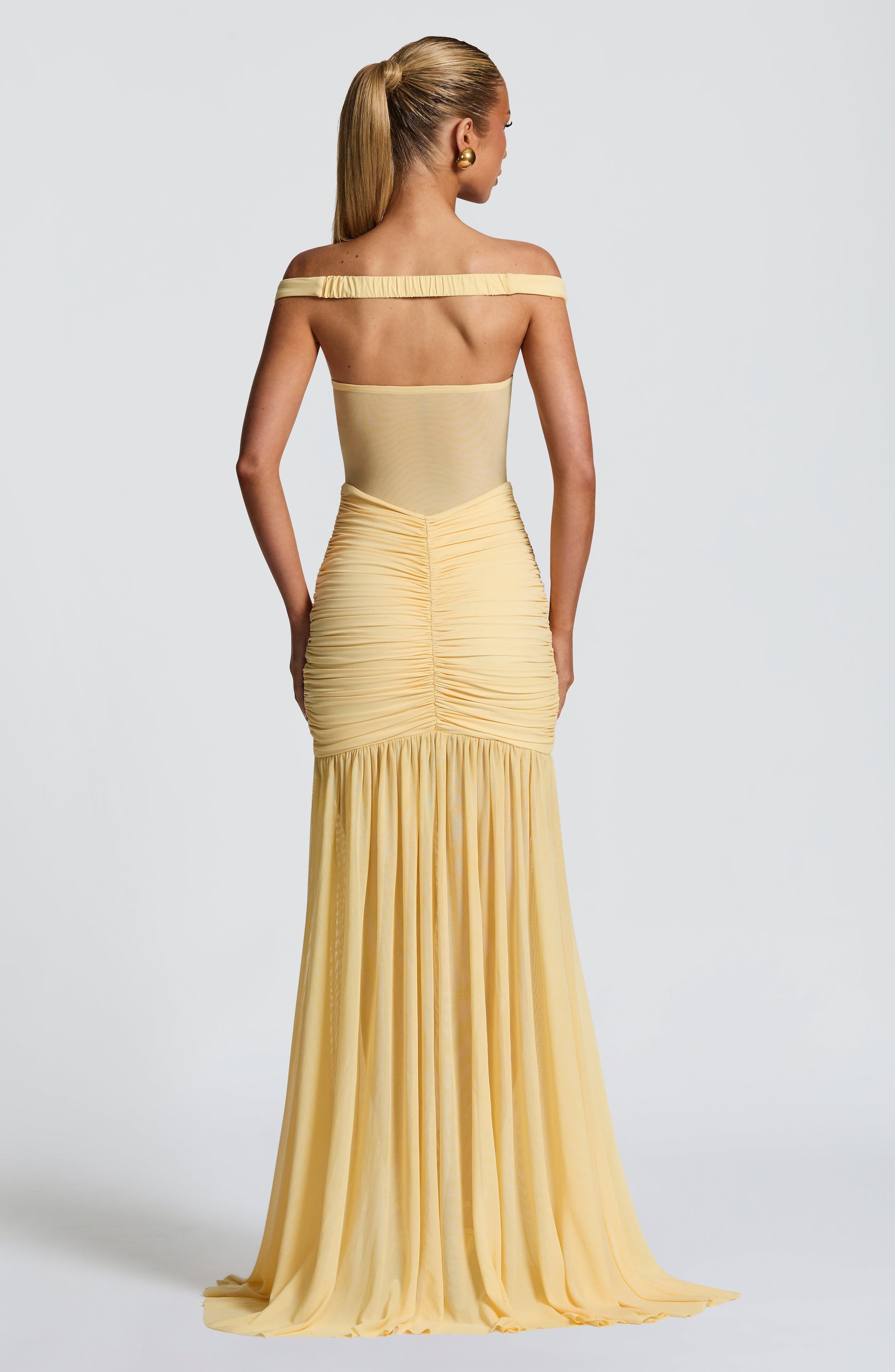 Woman wearing a yellow off-shoulder gown on a light gray background