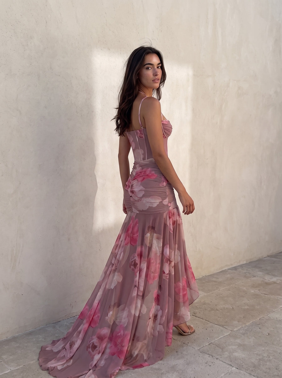 Woman walking away in the blurred floral gown, glancing back, the fishtail train trailing across the stone floor — SÉRAPHINE CORSET GOWN — Kalii