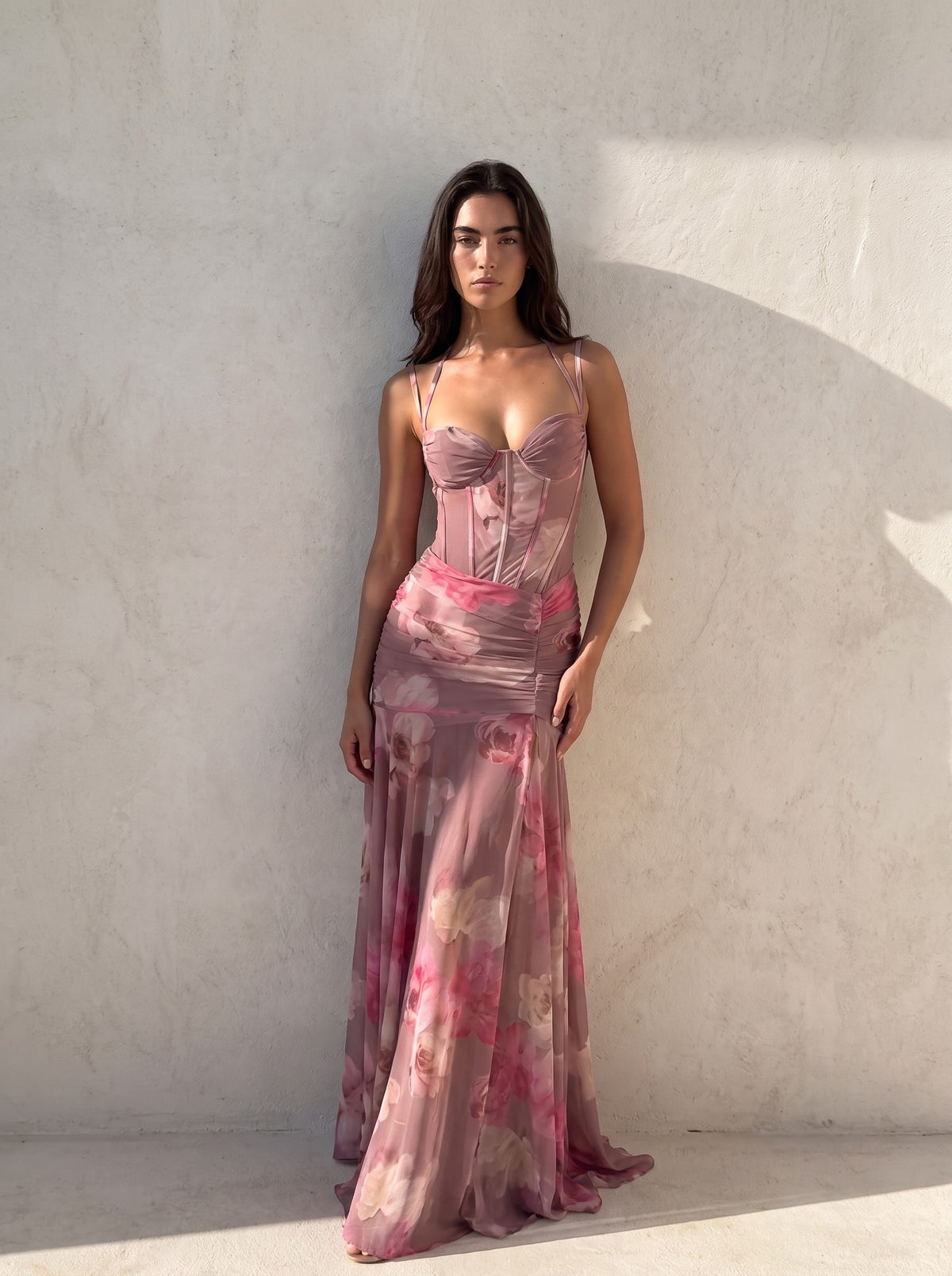 Woman in a dusty mauve blurred floral corset gown against a sunlit plaster wall, boned bodice and ruched waist visible — SÉRAPHINE CORSET GOWN — Kalii