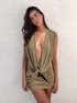 Woman wearing an olive green drape mini dress with deep V neckline, standing against a white studio wall — Kalii