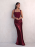 VESPERA BEADED GOWN in burgundy — leaning against a sun-washed plaster wall — Kalii